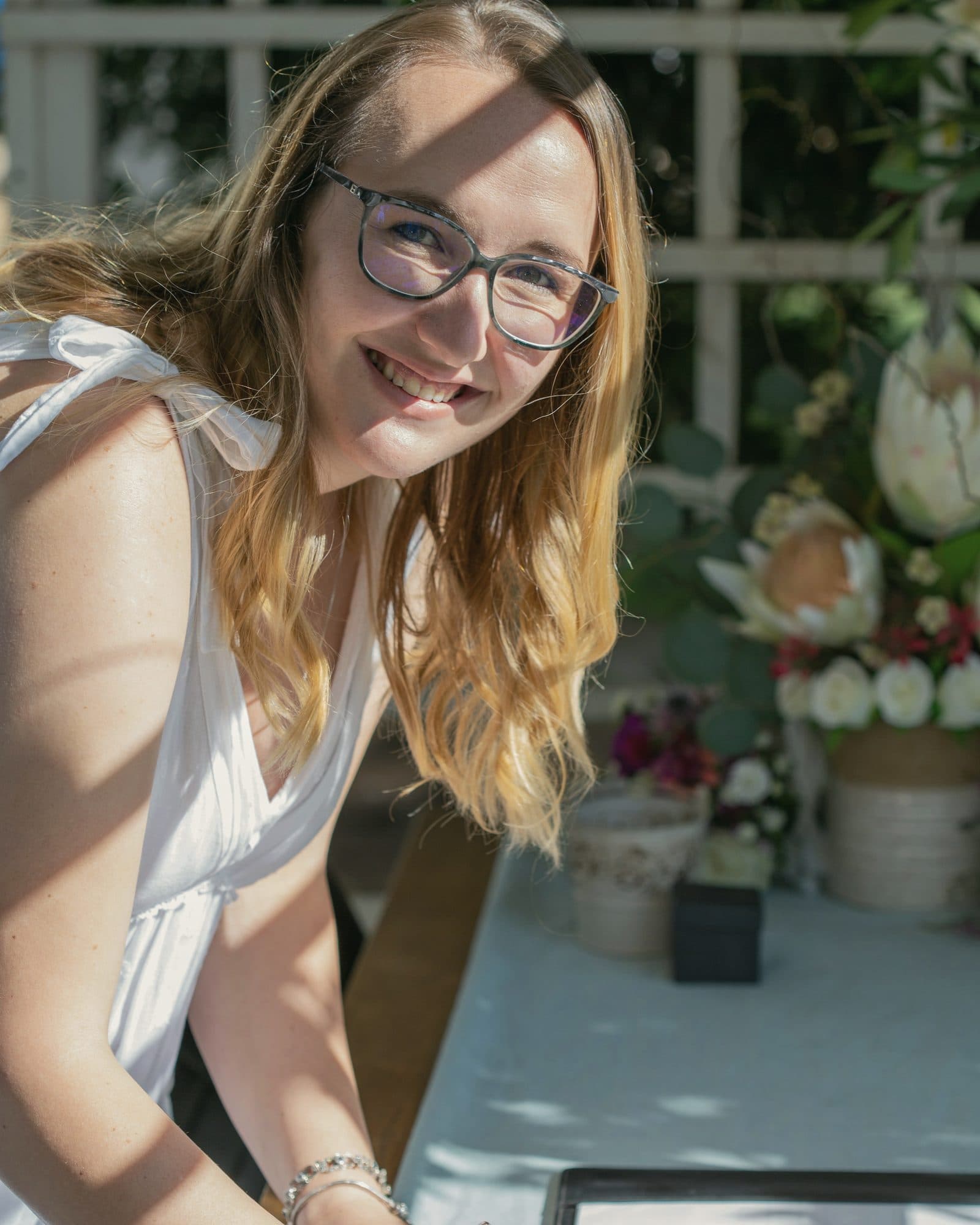Wedding planner sonriente atendiendo los detalles de una mesa con flores al aire libre.
